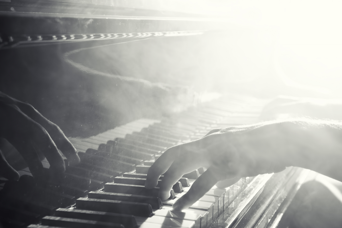 Black and white photo; closeup of hands playing piano in a smoke filled room